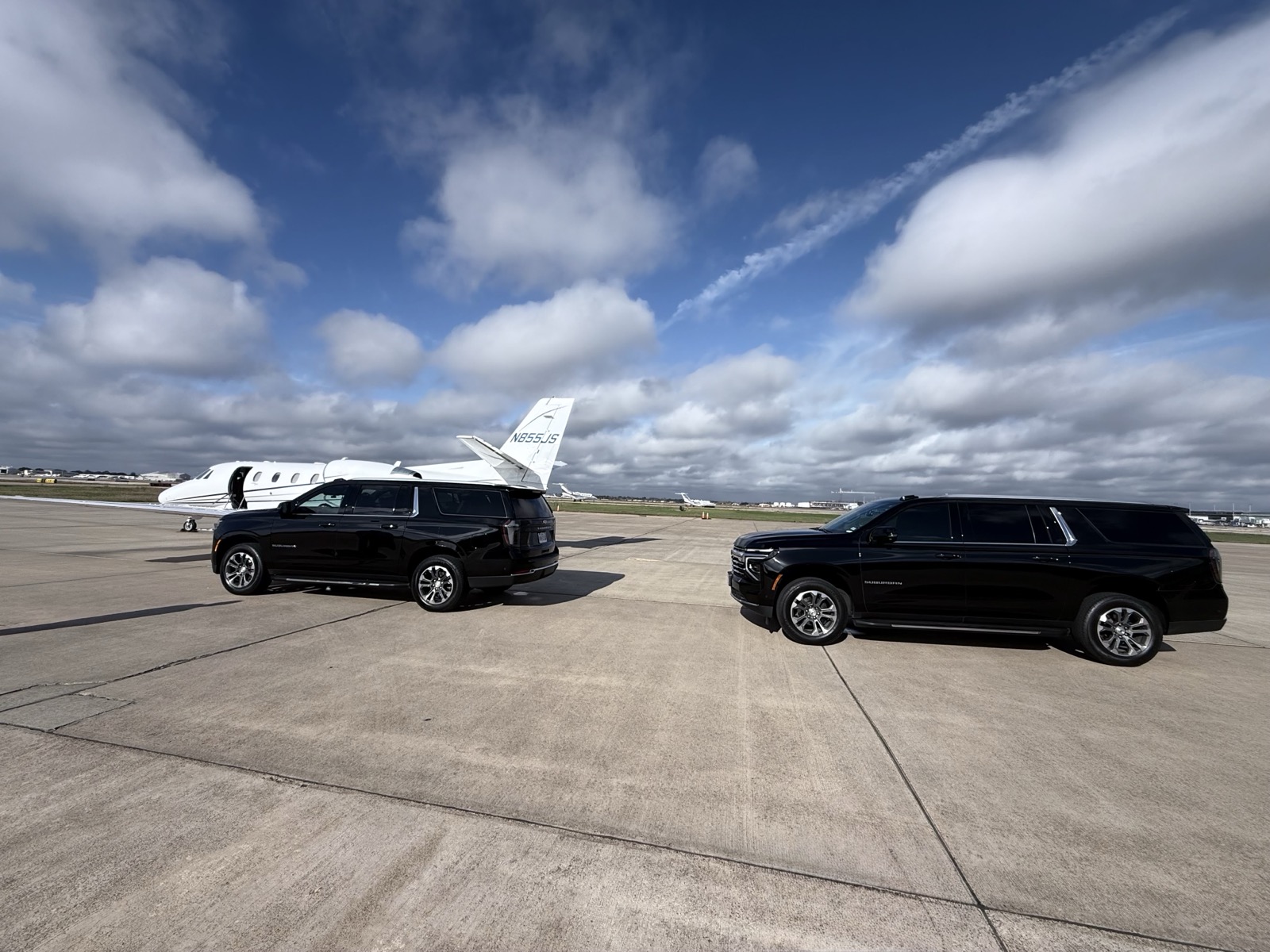 Two luxury SUVs on tarmac with private jet